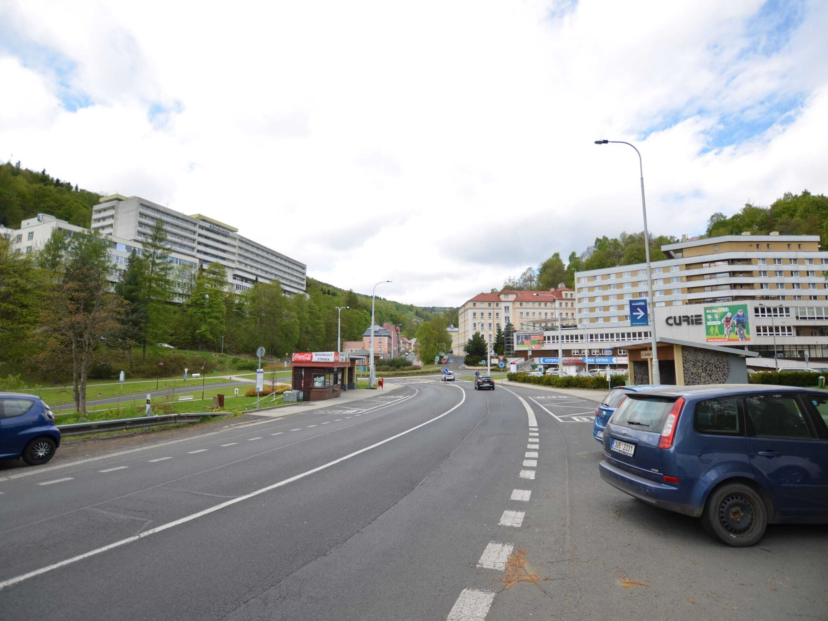 Una carretera con varios carriles, vehículos, un quiosco de Coca-Cola y edificios, incluyendo un hotel llamado CURIE.