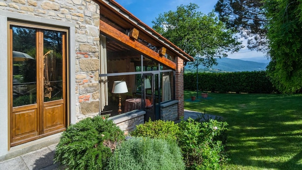 A stone building with a wooden porch, large windows, and a view of a green landscape. - Belvilla by OYO Gallorimpi (Dicomano)