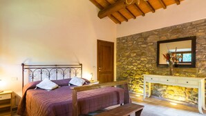 A bedroom with a bed, a bench, a nightstand, a dresser, and a stone wall. - Belvilla by OYO Gallorimpi (Dicomano)