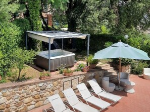A hot tub under a pergola, surrounded by stone walls and potted plants.