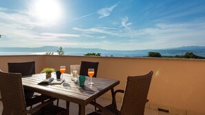 A terrace with a table set for two, overlooking a scenic view of the sea and mountains. - Apartment in Omisalj Near Sea Beach (Omisalj)