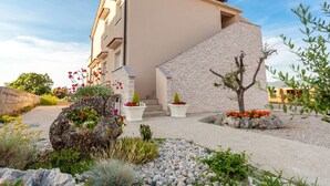A modern building with a stone facade, a small garden with potted plants, and a clear blue sky. - Apartment in Omisalj Near Sea Beach (Omisalj)