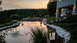 A serene pond with a stone border, surrounded by lush greenery and a modern building with outdoor seating. - Comfy Holiday Home in Bunjevci With Hot Tub (Vrbovsko)