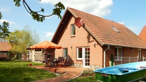 A brick house with a sloped roof, a patio with outdoor furniture, and a green boat parked in the driveway. - Ferienhaus in Neu Poserin for 5 Personen (Neu Poserin)