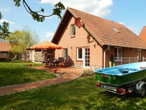 A brick house with a sloped roof, a patio with outdoor furniture, and a green boat parked in the driveway.