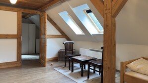 A loft bedroom with wooden beams, a skylight, a bed, a chair, and a table.