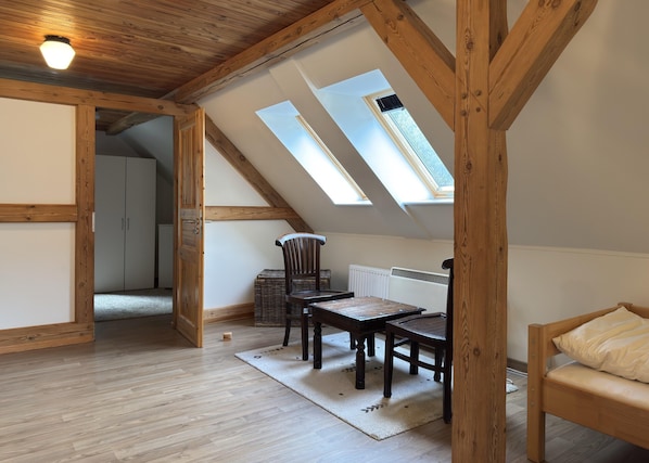 A loft bedroom with wooden beams, a skylight, a bed, a chair, and a table. - Ferienhaus in Neu Poserin for 5 Personen (Neu Poserin)