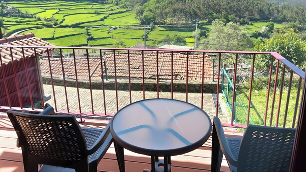 Een balkon met een tafel en stoelen met uitzicht op een terrasvormig, groen landschap.
