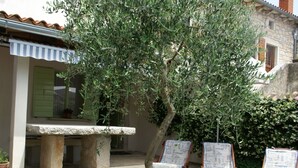 An outdoor seating area with a stone table and two wooden chairs, surrounded by a flower bed. - Stone Holiday Home in Peresiji With Pool (Svetvincenat)