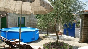A pool area with a blue pool, wooden lounge chairs, an umbrella, and a stone building with a green door. - Stone Holiday Home in Peresiji With Pool (Svetvincenat)