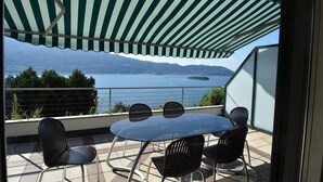 Eine Terrasse mit Tisch und Stühlen mit Blick auf ein Gewässer und Berge.
