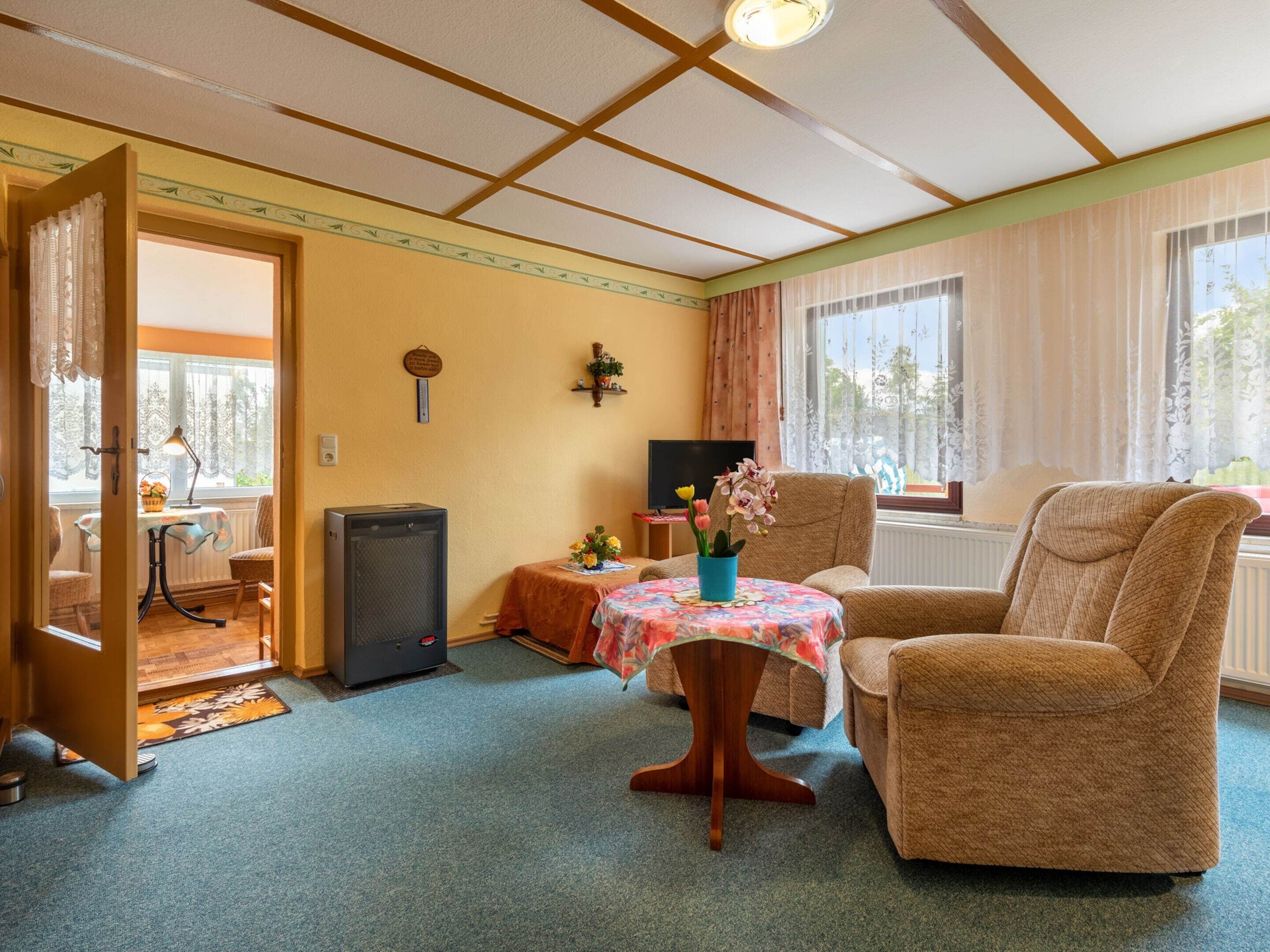 A cozy room with a wooden ceiling, a sofa, a small table with a floral tablecloth, and a television on a stand.