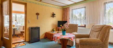 A cozy room with a wooden ceiling, a sofa, a small table with a floral tablecloth, and a television on a stand.