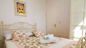 Een bed met bloemenbeddels, een wit hoofdeinde en een schilderij aan de muur.