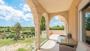 A balcony with a glass table and wicker chairs, overlooking a landscaped garden and a clear sky. - Modern Home in Quiet Pristeg (Benkovac)