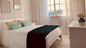 Une chambre à coucher bien rangée, avec un lit, une table de chevet, une commode et une fenêtre avec des rideaux.