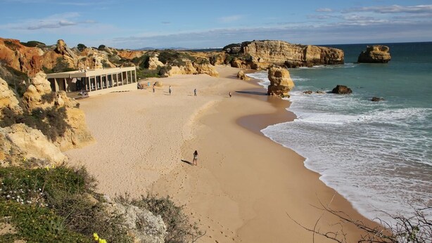 Une plage avec un bâtiment, des falaises rocheuses et un ciel dégagé.