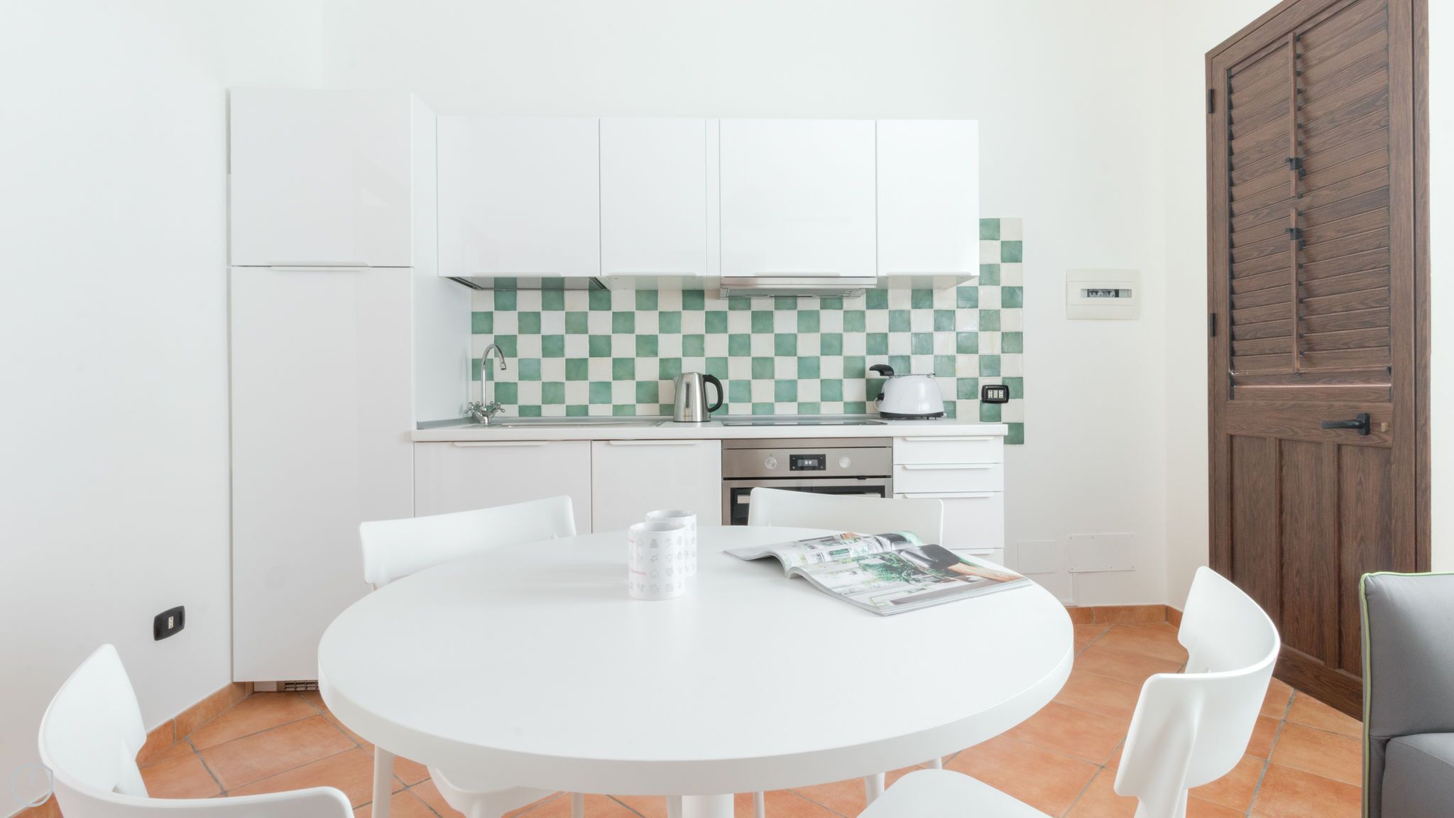 A compact kitchen with white cabinets, a checkered backsplash, and a round dining table with chairs.