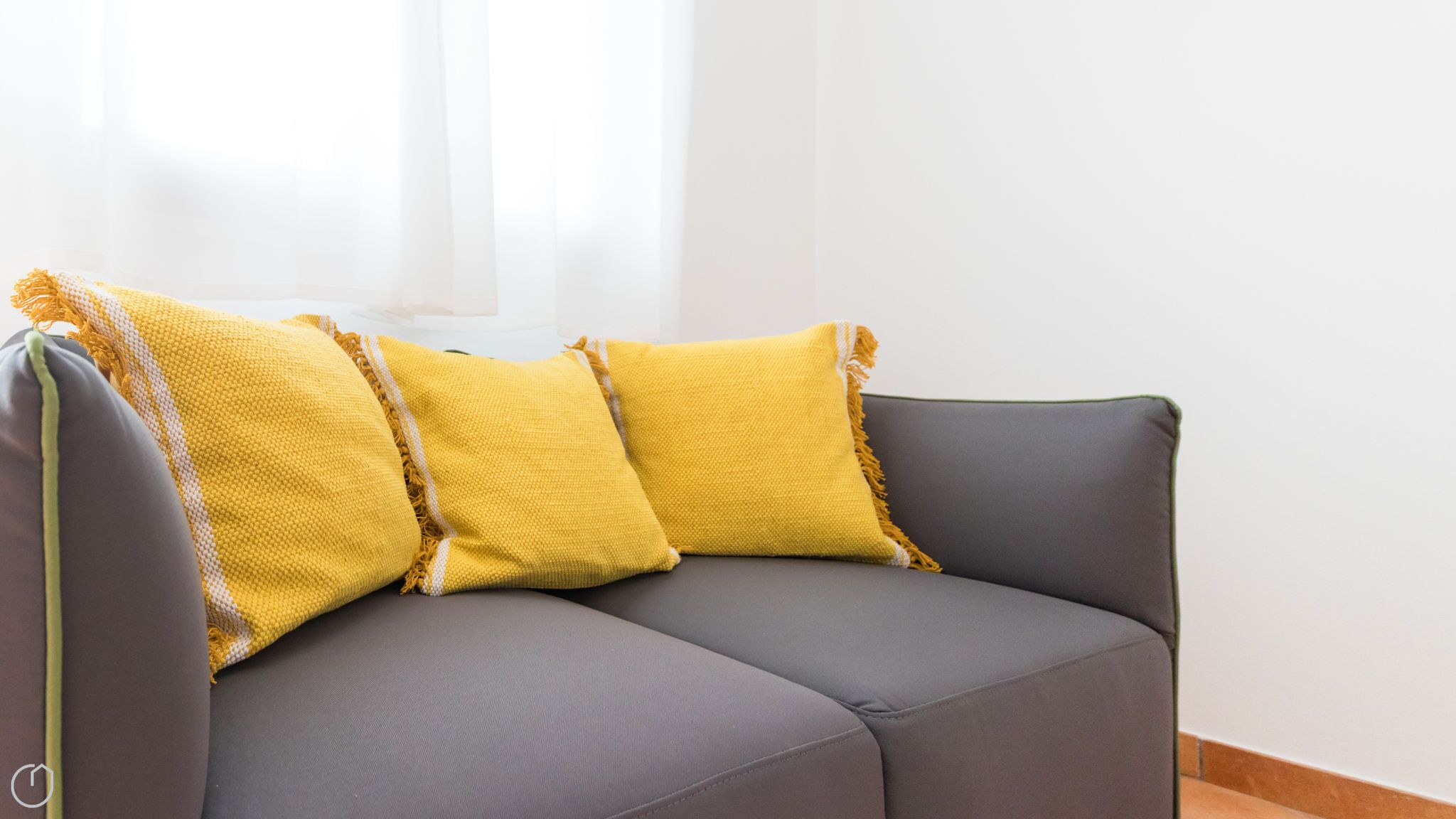 A grey sofa with yellow pillows against a white wall.