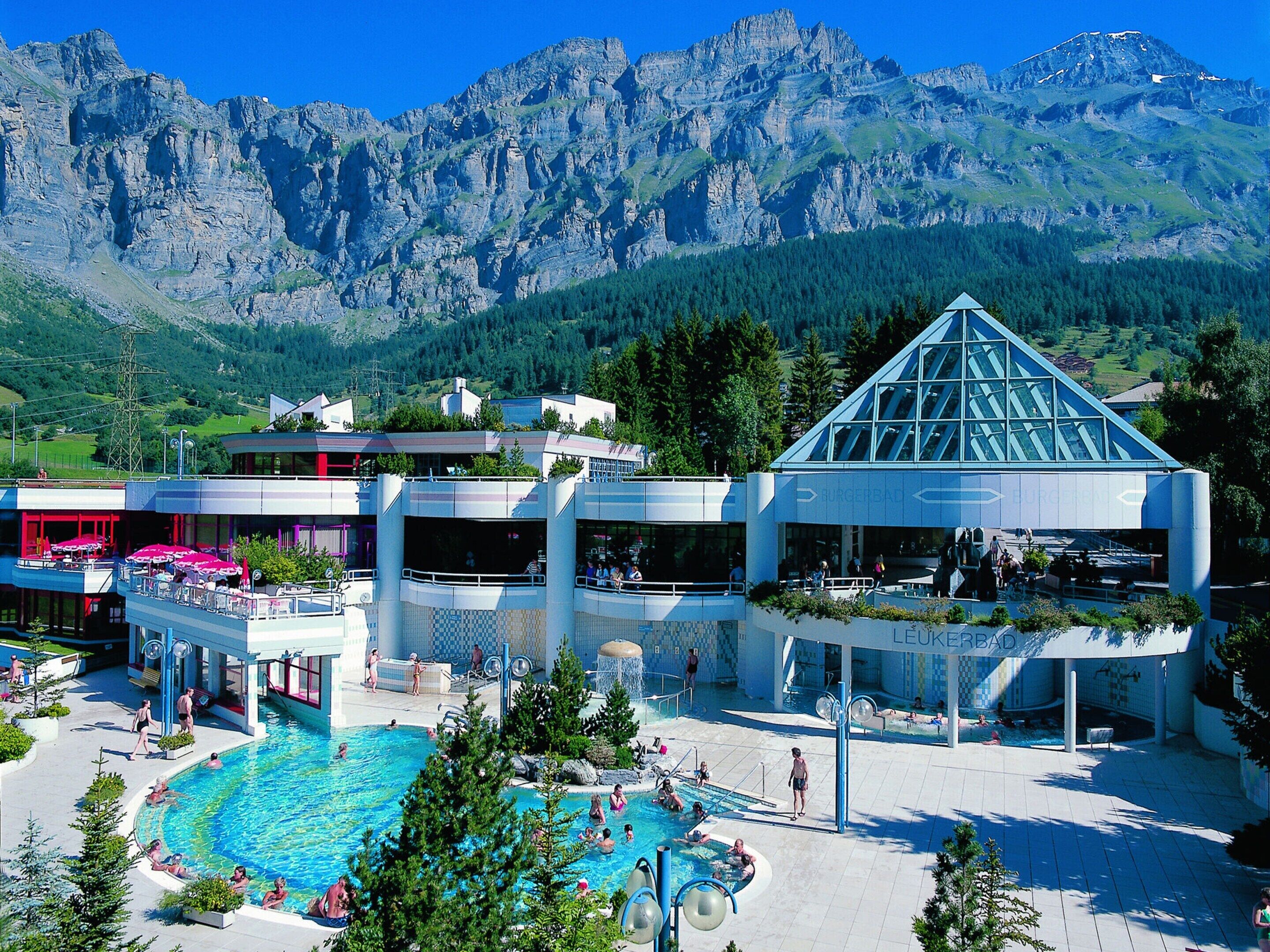 A hotel with a pool area, outdoor seating, and a view of mountains.