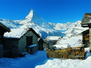 A snow-covered mountain village with traditional stone buildings and a prominent mountain peak in the background.
