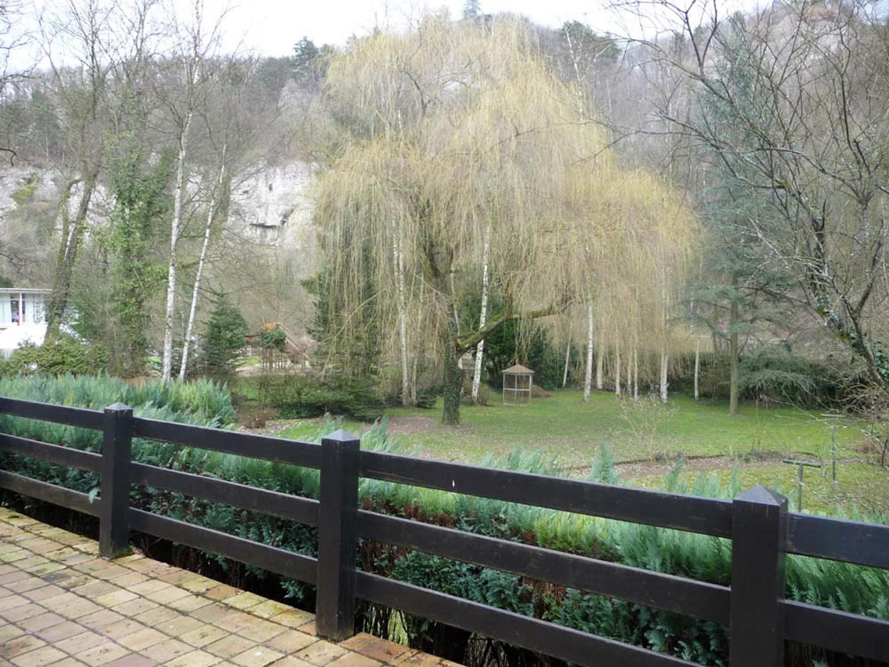 A wooden deck with a view of a garden, a gazebo, and trees.