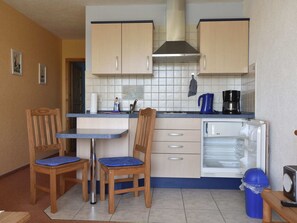 Cocina compacta con dos sillas de madera, una mesa pequeña, cafetera y lavavajillas.
