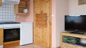 Eine kompakte Küche mit Herd, Backofen und einem Fernseher auf einem Holzständer.