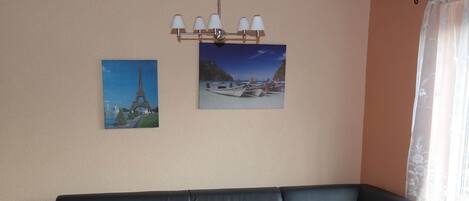 A living room with a black leather sofa, a small table with a decorative item, and two framed pictures on the wall.
