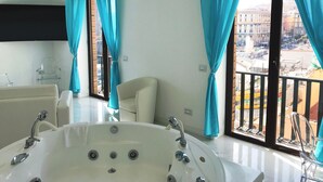 Un baño moderno con una bañera grande, un inodoro y un lavamanos. Hay dos sillas y un balcón con vistas a la ciudad.