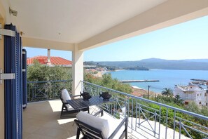 A balcony with a table and chairs, overlooking a coastal view with a pier and buildings. - Villa in Finikounta Near Sandy Beach (Pylos-Nestoras)