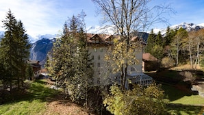 A traditional chalet with a sloped roof, surrounded by trees and a mountain backdrop. - Apartment Belvedere (Lauterbrunnen)