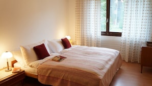 A neatly made bed with a striped blanket, two pillows, a bedside lamp, and a book on the nightstand. - Apartment Belvedere (Lauterbrunnen)
