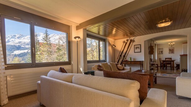 A cozy living room with a large window offering a mountain view, a wooden ceiling, and a dining area with a chandelier. - Apartment Belvedere (Lauterbrunnen)