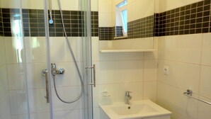 Un bagno con cabina doccia in vetro, un lavandino bianco e uno specchio sopra il lavandino.