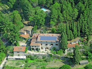 Vista aérea de um bairro residencial com várias casas, uma piscina e um prédio grande com painéis solares.