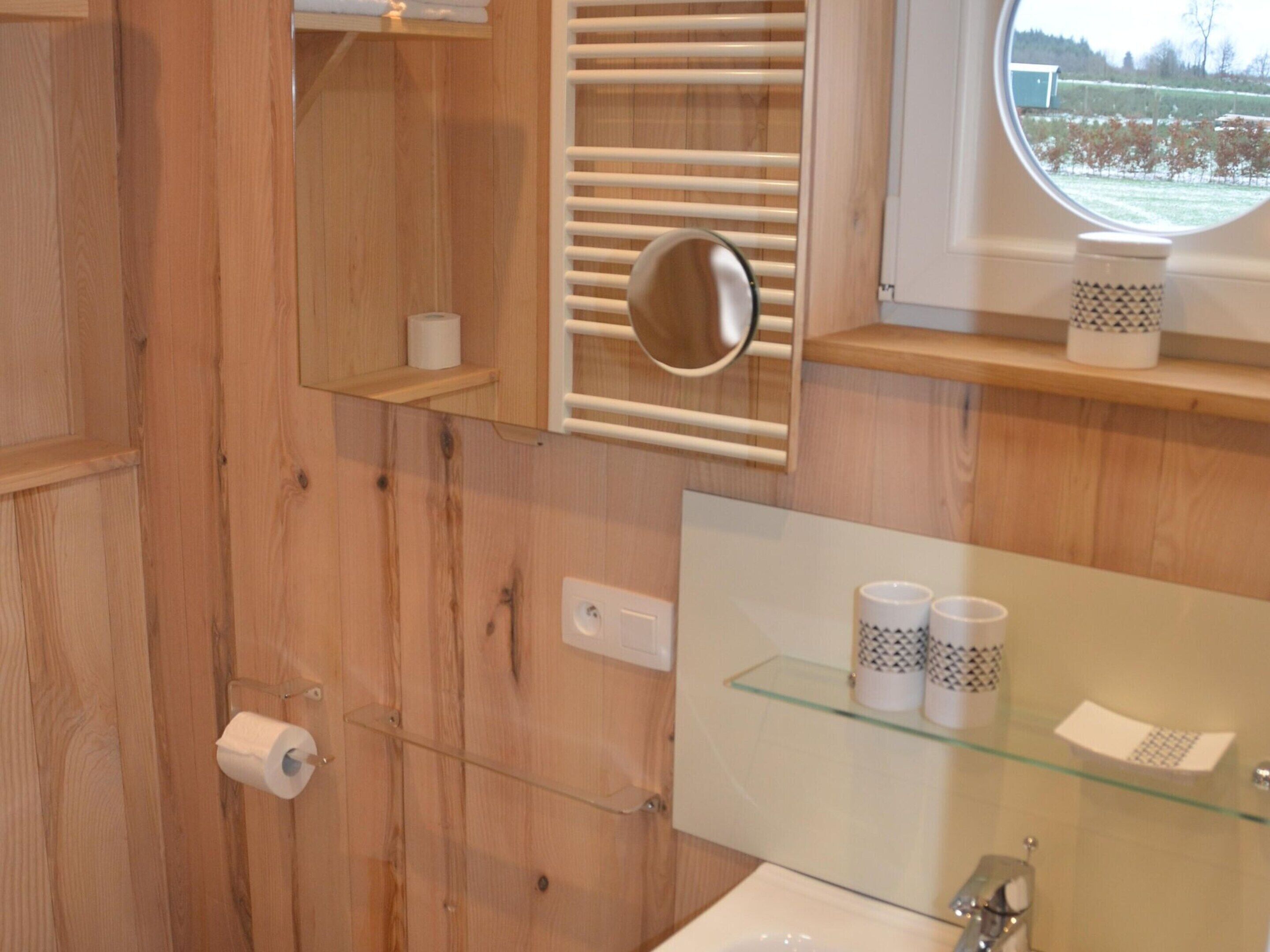 Ein Badezimmer aus Holz mit einem Glastischchen für Toilettenartikel, einem Handtuchhalter und einem Fenster mit Blick auf einen Weinberg.