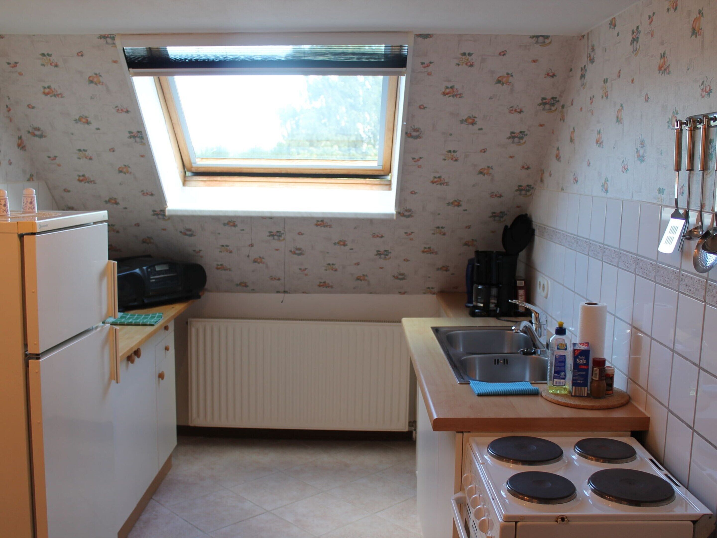 Een kleine keuken met raam, fornuis, spoelbak en koelkast.