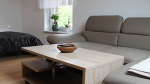 Moderni olohuone, jossa on vaaleasta puusta valmistettu sohvapöytä, harmaa sohva ja tummanvärinen sänky.