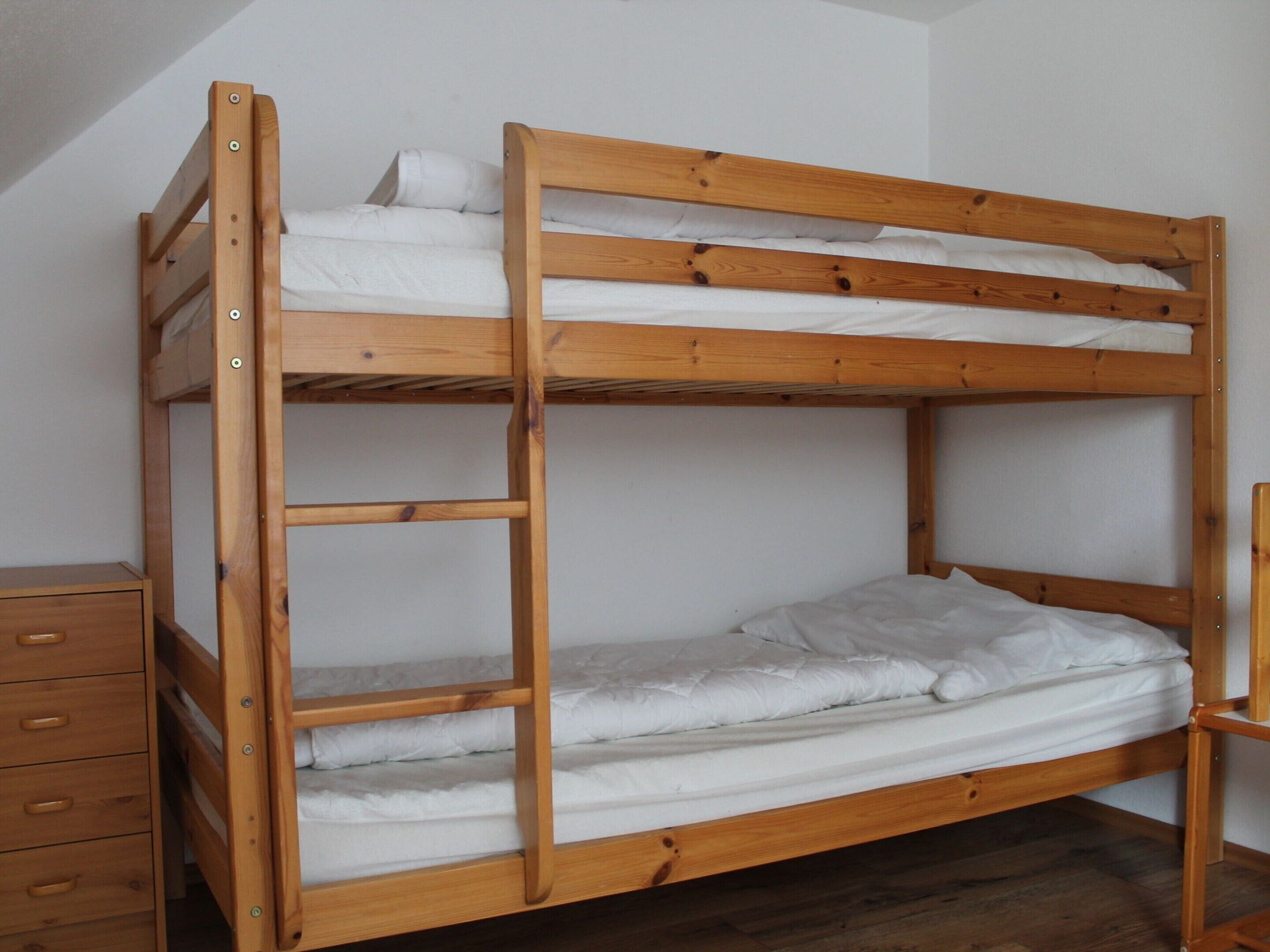 Un lit superposé avec une structure en bois, une literie blanche et une commode en bois dotée de tiroirs.