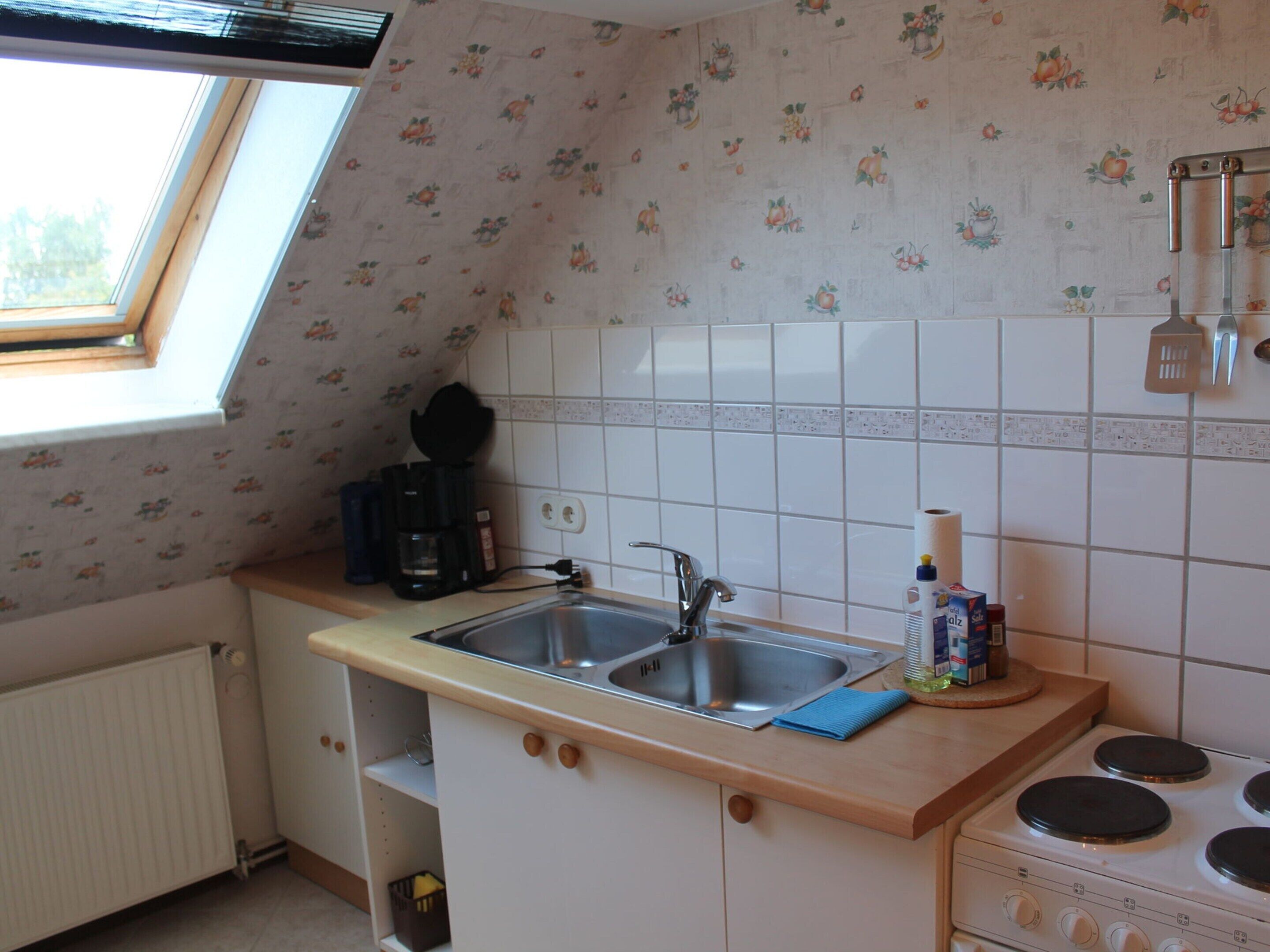 Ett kök med ett fönster, en diskho, en spis och en kaffebryggare.