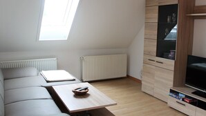 A modern, compact living space with a sloped ceiling, a built-in TV cabinet, and a small seating area with a table. - Lovely Apartment in Beckerwitz near Terrace (Hohenkirchen)