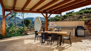 An outdoor patio with a wooden pergola, a stone centerpiece, a barbecue grill, and a table with chairs. - Villa in Sicily Near Guidaloca Bay (Castellammare del Golfo)