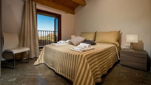 A bedroom with a bed, a chair, a nightstand, a window with curtains, and a view of the landscape. - Villa in Sicily Near Guidaloca Bay (Castellammare del Golfo)