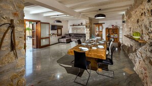 A spacious dining area with a wooden table set for six, surrounded by stone walls and a high ceiling with exposed beams. - Villa in Sicily Near Guidaloca Bay (Castellammare del Golfo)