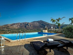 A pool with clear blue water, surrounded by lounge chairs and a mountain view. - Villa in Sicily Near Guidaloca Bay (Castellammare del Golfo)