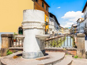 A historic fountain with intricate carvings, surrounded by a stone balustrade, set against a backdrop of colorful buildings and a canal.