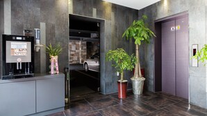 A modern lobby with a coffee machine, potted plants, and an elevator. - Aria Motel (Busan)