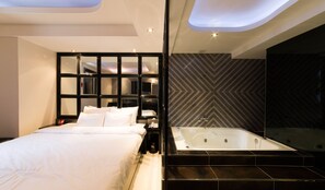A modern hotel room with a large bed, a separate bathroom with a bathtub, and a unique ceiling design. - Aria Motel (Busan)