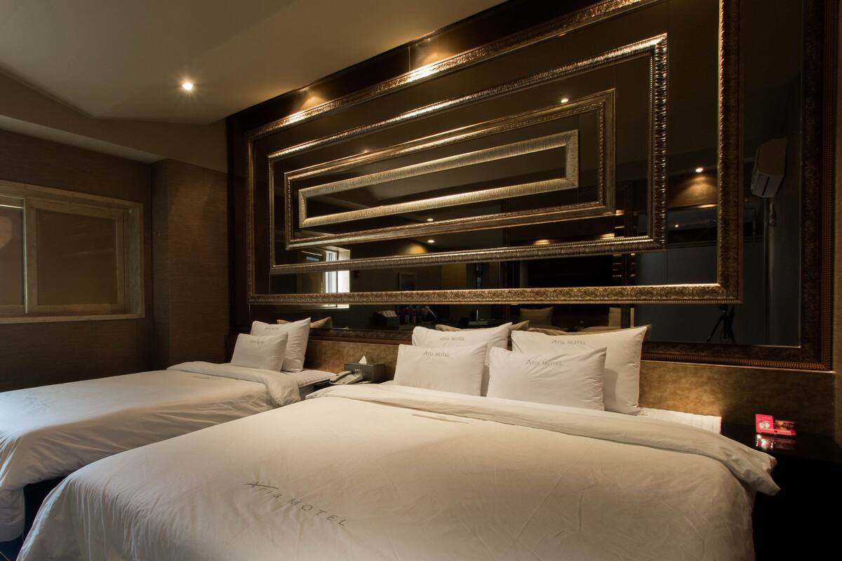A hotel room with two beds, a large mirror, and a window.